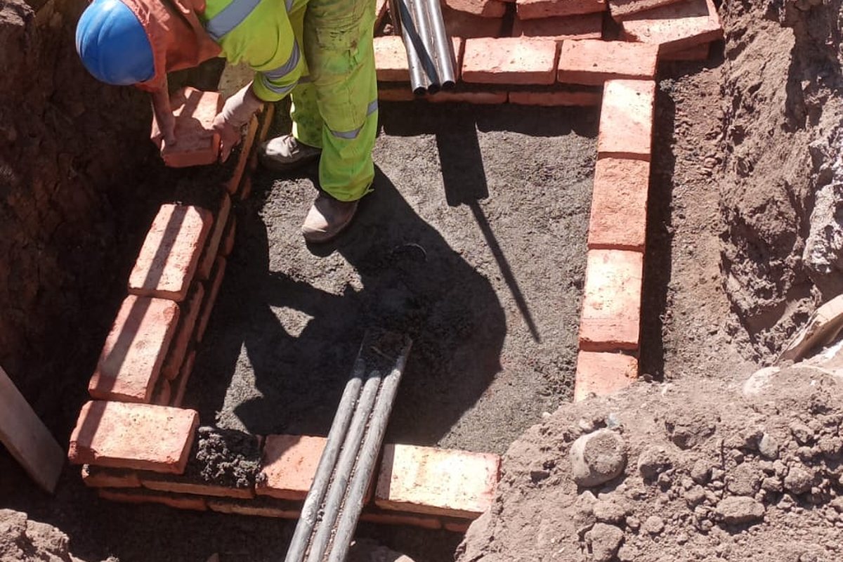 Cámara de paso levantada en ladrillo, con los ductos ya entrando por el costado de la excavación.