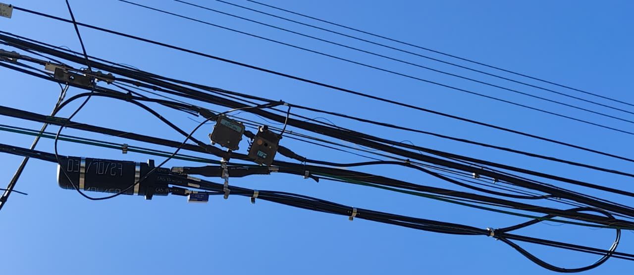 Mufa instalada en una línea aérea de fibra en Providencia, con la reserva de cable enrollada a un costado y el tendido completo recortado contra el cielo.